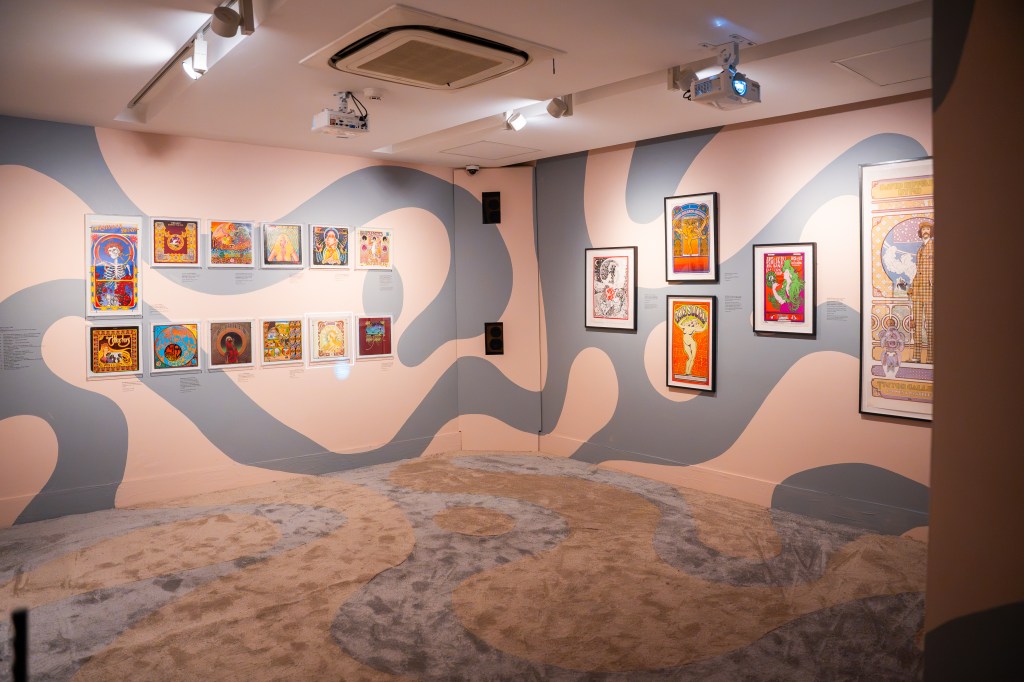 Sala de exposición con ilustraciones enmarcadas en las paredes y patrones de color en el fondo.
