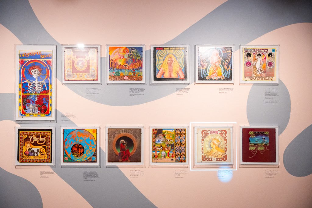 Exposición de portadas de álbumes enmarcadas, presentando arte colorido y variado, en una pared con fondo rosa.